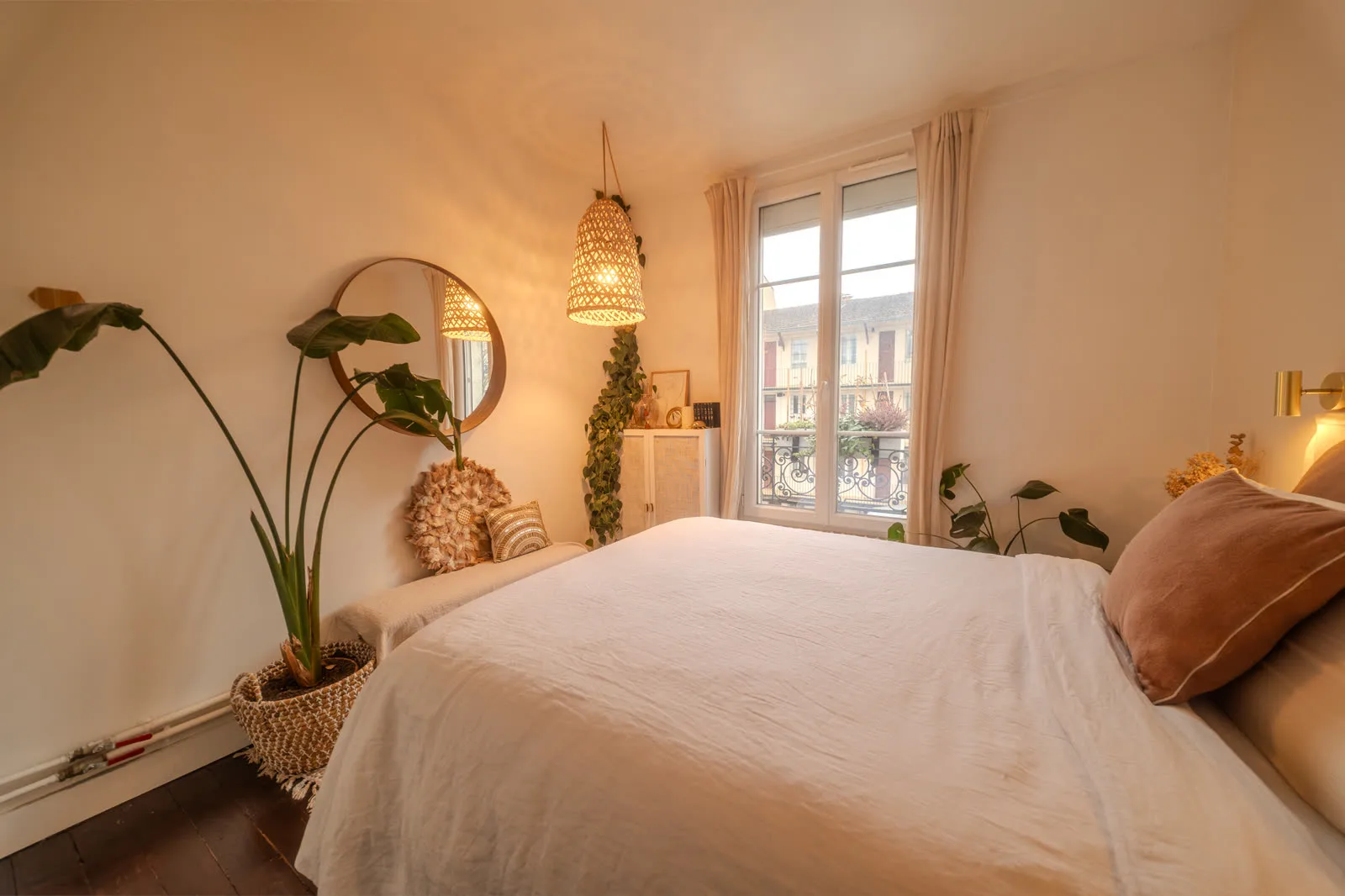 Chambre chaleureuse de l'appartement parisien — lit blanc et lumière dorée.